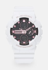 Montre G-Shock avec un bracelet en résine blanche et un cadran noir, accents roses, écran numérique et plusieurs cadrans pour les fonctions d'heure et de date.