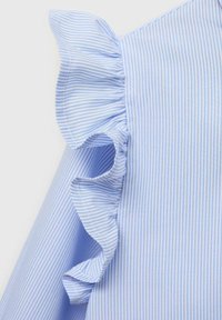 Vaaleansininen raidallinen paita, jossa on liehitsevi accentti olkapäällä. Kangas on sileä, jossa on hienoja raitoja ja pehmeä tekstuuri.