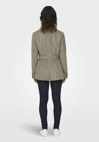 Khaki gebonden blazer met een getailleerde pasvorm, gestructureerde stof, enkele rugsplit, gecombineerd met donkere jeans en witte sneakers.