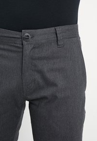 Grijze denim broek met knoopsluiting, vlakke voorkant en zakken. De stof heeft een gladde textuur met een subtiel gemêleerd patroon.