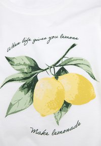 Vit bomullströja med tryck av två gula citroner på gröna blad. Texten lyder "När livet ger dig citroner / Gör lemonad."