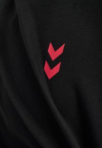 Svart tyg med en slät, matt textur och en framträdande röd chevronlogotypdesign på sidan.