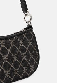 Borsa a mano in tessuto nero con motivo geometrico beige, rifiniture in pelle nera, anelli in argento e tracolla staccabile su sfondo bianco.