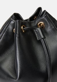 Saco de cordão em couro preto com ilhoses em tom dourado e uma superfície texturizada. Forma suave e arredondada com um design de topo gathered.