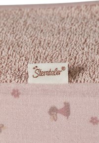 Soft pink towel featuring a textured, fluffy top and a smooth, patterned bottom with small floral designs. Includes a branded woven label.