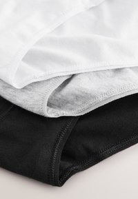 Pile de trois sous-vêtements en coton blanc, gris et noir, montrant un gros plan des bords cousus et de la texture du tissu.