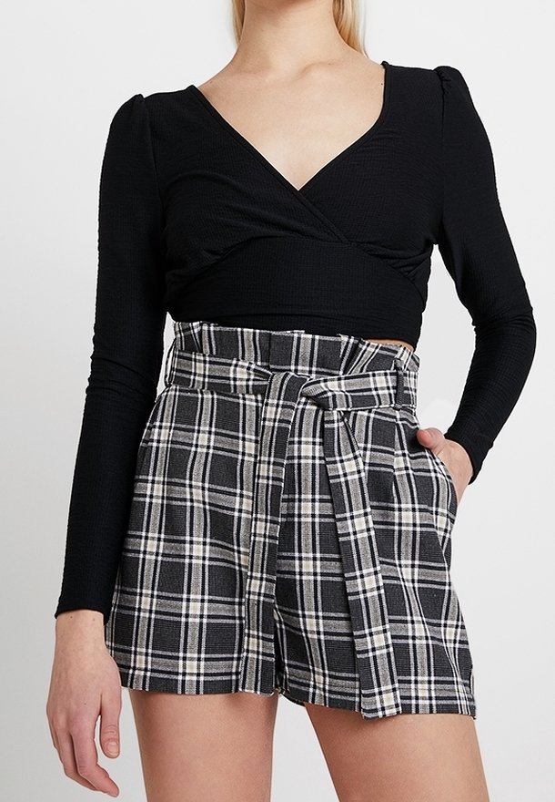 Schwarzes Langarm-Wickeloberteil kombiniert mit hochgeschnittenen karierte Shorts, die einen Gürtel haben, in Schwarz und Weiß, mit einer weichen Textur.