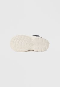 Αθλητικά παπούτσια με υφασμένο μαύρο επάνω μέρος, λευκή μέση σόλα και λαστιχένια εξωτερική σόλα με μοτίβο πρόσφυσης για καλύτερο κράτημα.