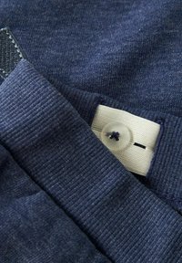 Tejido azul marino con una superficie texturada y bordes acanalados; cuenta con un botón blanco y costuras reforzadas para mayor durabilidad.