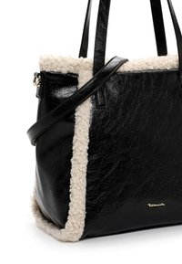 Black tote bag with soft white shearling trim, featuring textured faux leather, flat handles, and a gold logo accent on the front.