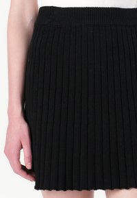 Jupe tricotée noire à côtes avec une taille élastique, présentant un motif vertical texturé et un ourlet à cru.