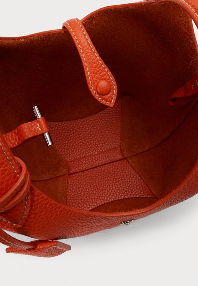 Notranjost oranžne usnjene torbice z reliefno teksturo, gladkim dnom, zapiranjem na patent in majhnim kovinskim zatičem.