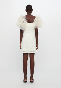 Weißes Spitzenkleid mit durchsichtigen, gepufften Tüllärmeln. Figurbetonte Form, knielanger Saum. Glatte Textur und zartes florales Muster.