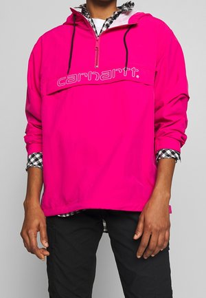 Felpa rosa con zip a metà colletto, caratterizzata da un logo frontale, polsini elasticizzati e una camicia a quadri a strati sotto.