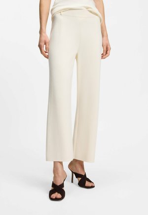 Woman wearing cream wide-leg pants paired with black high-heeled sandals against a white background.
