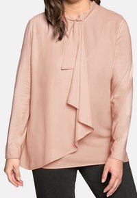 Rosa blus i blush-pink med draperad front, mjuk och slät textur, långa ärmar och knytning vid halsen. Matchade med svarta byxor.