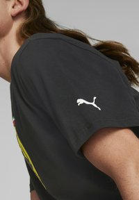 Camiseta de algodón negra con un logo blanco de Puma en la manga izquierda, con cuello redondo y mangas cortas.