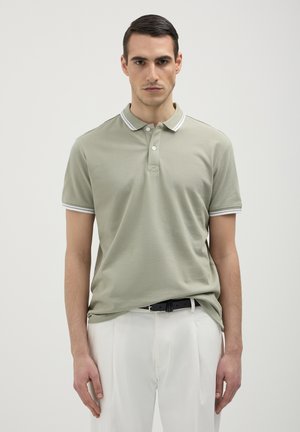 Polo en tissu vert clair, avec un col classique, une patte de boutonnage à trois boutons et des accents rayés blancs sur le col et les manches.