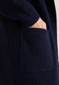 Granatowy sweter z dzianiny o ryflowanej fakturze, z długimi rękawami i przednią kieszenią. Miękka tkanina o przytulnym, ciepłym wyglądzie.
