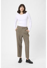 Witte lange mouwen top gecombineerd met bruine geruite broek met een relaxed fit en diepe voorkruiken, aangevuld met zwarte schoenen.