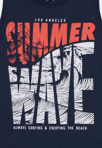 Canottiera navy con testo in bold rosso e bianco: "SUMMER WAVE" con illustrazioni di onde oceaniche e "ALWAYS SURFING & ENJOYING THE BEACH" sottostante.
