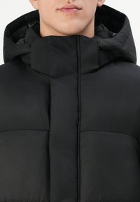Schwarze gepolsterte Jacke mit hohem Kragen und verstellbarem Kapuze. Die Oberfläche hat eine glatte Textur mit horizontalen Nähten und einem matten Finish.