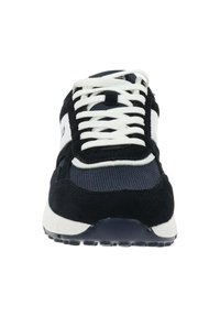 Zapatilla deportiva en blanco y negro con cordones blancos, parte superior de malla y ante, y suela de goma, vista desde el frente.