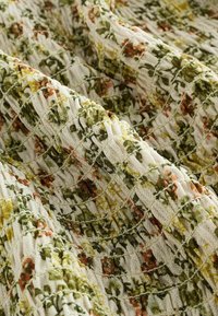 Tejido con estampado floral en tonos blancos, verdes y naranjas; superficie texturizada con costuras en forma de cuadrícula y una apariencia suave y tejida.
