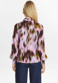 Långärmad blus i ett flytande tyg med ett mönster i rosa, brunt och grönt tie-dye; har en liten detalj på baksidan och rynkade manschetter.