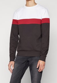 Bomulds-sweatshirt med hvid top, en rød vandret stribe samt mørkegrå ærmer og krop. Ribstrikkede manchetter og kant for pasform.