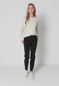 Cremefarbener Pullover, schwarze eng anliegende Hose und weiße Sneakers. Der Pullover hat eine strukturierte Oberfläche; die Hose hat ein dezentes Taschen-Design.