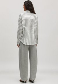 Witte shirt met zwarte verticale strepen, rugplooien en een puntige kraag, gecombineerd met grijze wijde sweatpants en hakken.