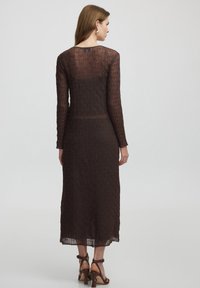 Langes, tailliertes Kleid aus strukturiertem braunem Stoff mit einem gemusterten Design. Es hat lange Ärmel und einen runden Ausschnitt.