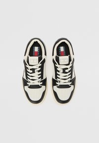 Paire de baskets Tommy Jeans noires et blanches avec lacets, zone des orteils perforée et semelle intérieure brandée, vues de dessus sur un fond clair.