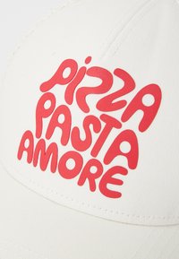 Bela kapa z zadovoljeno teksturo, ki ima na sprednji strani izrazito rdečo napisano "PIZZA PASTA AMORE" v igrivem fontu.