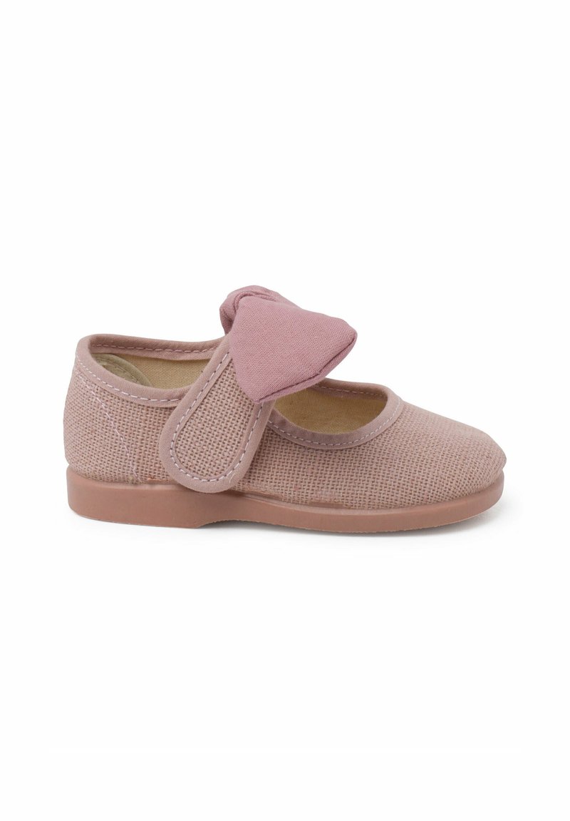 Zapato de tela rosa claro con un diseño texturado, punta redondeada y una gran tira de velcro en forma de lazo en el lateral. Suela plana de goma.