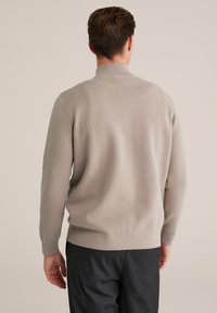 Hellegrauer Strickpullover mit Stehkragen, gerippten Bündchen und Saum. Weiche Textur mit figurnaher Passform, kombiniert mit dunkelgrauen Hosen.