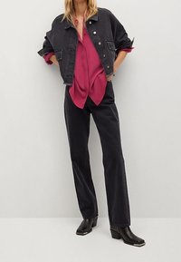 Schwarze Jeansjacke, fuchsia Bluse, schwarze Jeans und Ankle Boots. Die Jacke hat ein kurzes Design mit sichtbaren Knöpfen und Taschen.