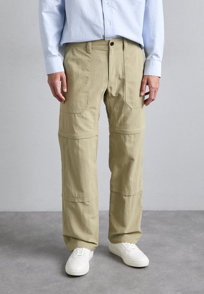Khaki Cargo-Shorts mit mehreren Taschen, einer lockeren Passform und einer glatten Textur, kombiniert mit weißen Sneakers und einem hellblauen Hemd.