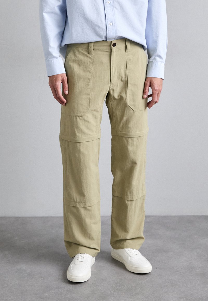 Pantalons cargo couleur khaki avec plusieurs poches, une coupe décontractée et une texture lisse, associés à des baskets blanches et une chemise bleu clair.