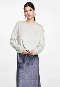 Vaaleanharmaa neule tarkasti leveällä kaula-aukolla ja pitkillä hihoilla, yhdistettynä kiiltävään tummansiniseen kukkakuosiseksi hameeksi, jossa on kiristysnauha.