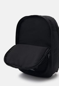 Mochila de tela negra con forma redondeada y cierre de cremallera. El interior cuenta con un compartimento forrado suave, sin patrones o acentos visibles.