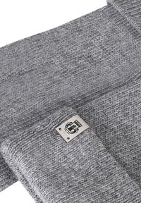 Grau gestrickter Schal mit einem gefalteten Ende, das ein genähtes beiges Etikett mit einem schwarzen Kronen- und Emblemdesign zeigt.