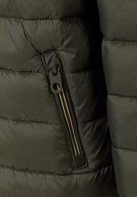 Olive green puffer jacket fabric with quilted pattern, featuring a zippered pocket with black zipper and yellow accent on the pull tab.