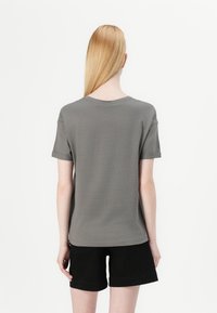 T-shirt gris à manches courtes avec un col rond, texture lisse et manches retroussées, associé à un short noir. Design simple.