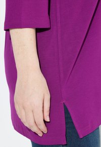 Lohkokangas paita, jossa on lyhyet hihat, sivurei'ät ja rento istuvuus, yhdistettynä tummansinisiin farkkuihin, jotka näyttävät tekstuuria ja ompeluyksityiskohtia.