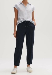 Vaaleansininen lyhythihainen paita, jossa on kaulus, napitettava etuosa ja tummansiniset naruhousut, joissa on sivutaskut. Valkoiset tennarit täydentävät asun.