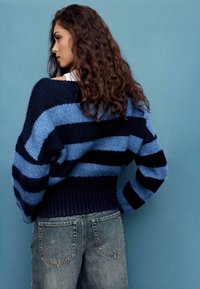 Gestrickter Pullover in Marineblau und Hellblau gestreift, mit breitem geripptem Saum und lockerem Schnitt. Kombiniert mit ausgewaschenen Jeans aus strukturiertem Stoff.