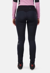 Schwarze Sporthosen mit hohem Bund, ausgestattet mit einer Reißverschlusstasche und genähten Details, kombiniert mit schwarzen Sport Schuhen.