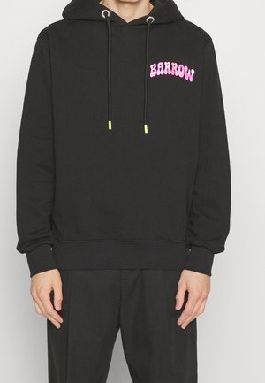 Sweat à capuche noir avec texte rose "BARROW" sur la poitrine, cordons avec embouts jaune néon, porté avec un pantalon noir, mains détendues sur les côtés.